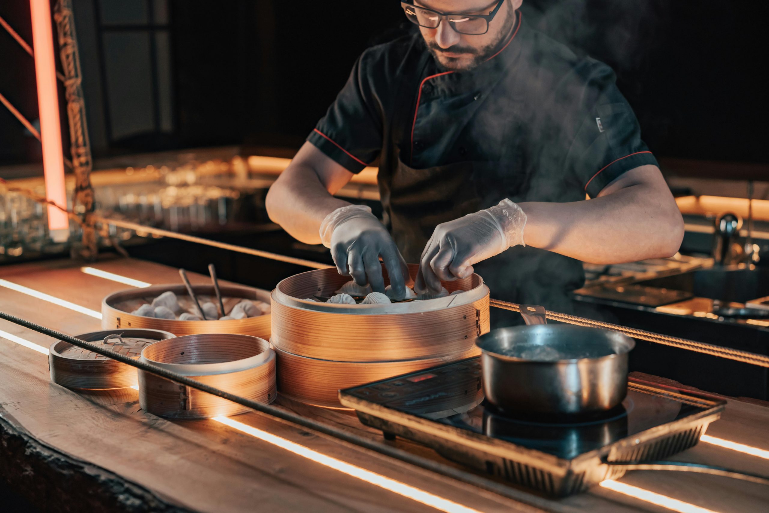 Chef cooking dumplings in bamboo steamers on a modern kitchen counter.